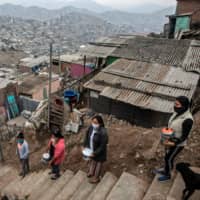 Women keep their distance from each other as they wait to get food at a soup kitchen on the outskirts of Lima on Thursday.  | AFP-JIJI