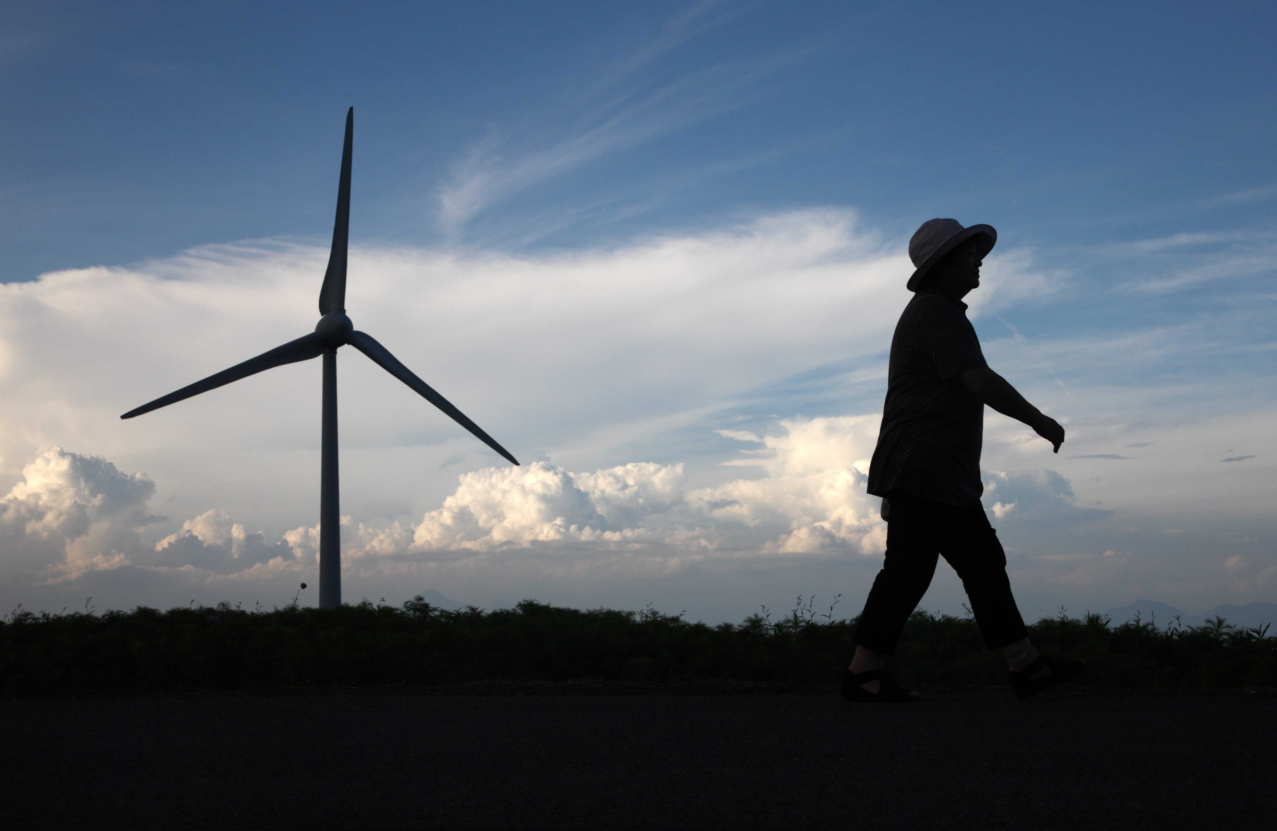 Propelled: A woman passes a turbine at the Electric Power Development Co. (J-Power) wind farm in Koriyama, Fukushima Prefecture, in August 2012. Investment in solar, wind and other clean energy sources has surged since the feed-in tariff system started in July 2012. | BLOOMBERG